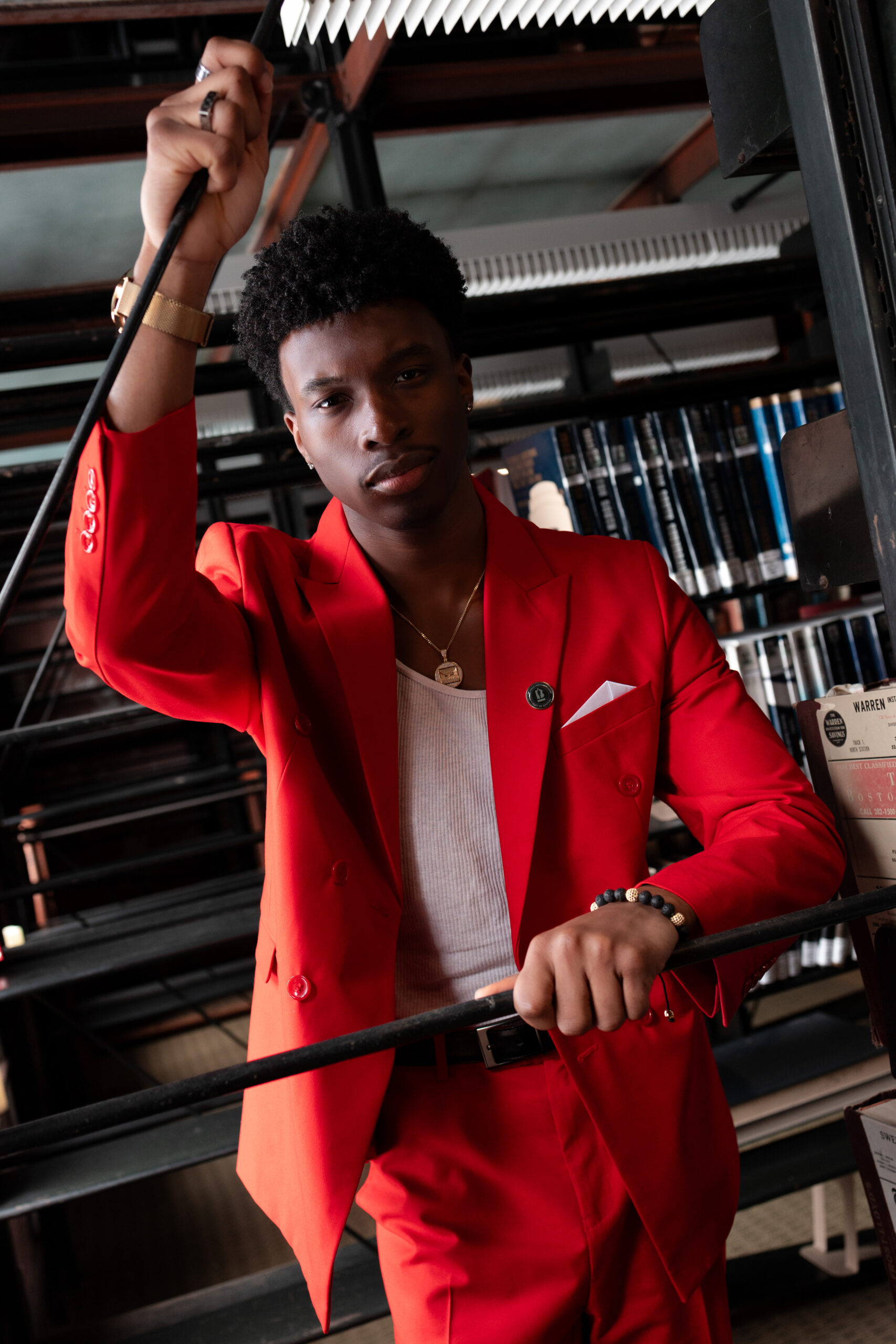Man in a red double-breasted suit leaning on a railing in library stacks