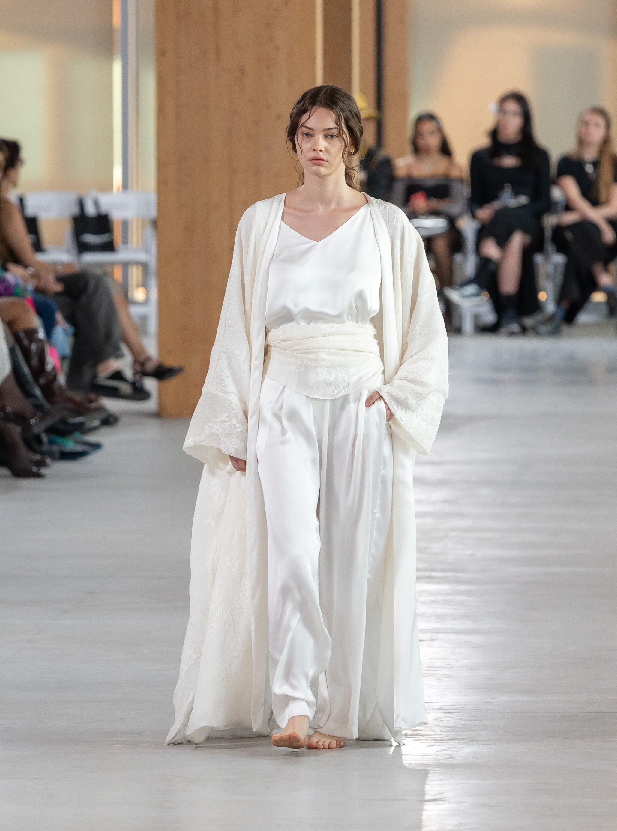 Model in an ivory robe and wide trousers walking barefoot